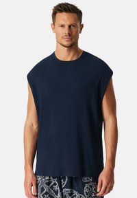 Donkerblauwe mouwloze T-shirt met een ronde hals en een ontspannen snit. Gemaakt van zachte, gestructureerde stof, met een strakke, minimalistische uitstraling.