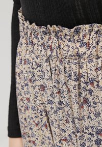 Rok van stof met bloemenpatroon in beige, marineblauw en rood. Beschikt over een geraffineerde tailleband en geplooid ontwerp. Close-up weergave van de materiaaltextuur.