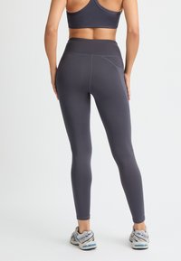 Graue Sportleggings mit hoher Taille, aus glattem, elastischem Material. Verfügen über flache Nähte und ein elegantes Design. Getragen mit Turnschuhen.