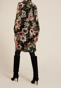 Vestido de estampado floral con fondo negro, mangas largas, cuello plisado y botas de tacón stiletto negras de ante hasta la rodilla.