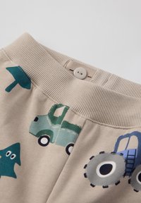 Beige bomulds-shorts med ribbet talje, der har grønne lastbiler, blå traktorer og et teal stjerneskrift mønster trykt på stoffet.