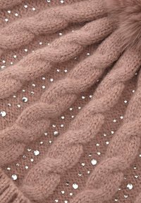 Gorro de punto cableado en suave lana rosa, con trenzas texturizadas y brillantes de cristal transparentes dispersos para un detalle visual adicional.