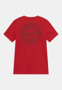 Punainen lyhythihainen t-paita, jossa on FC Bayern Münchenin logo painettuna tummemmalla punaisella takana.