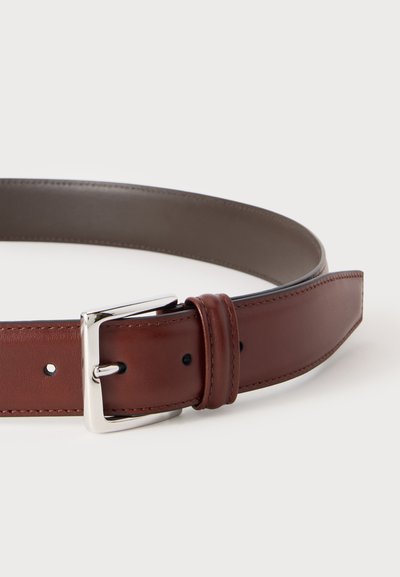 Ceinture en cuir marron avec boucle rectangulaire argentée et bords cousus, présentée enroulée sur un fond clair.