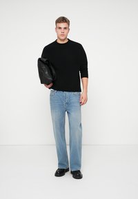 Suéter negro de punto, jeans rectos de color azul claro, zapatos negros y un bolso de cuero negro. Diseño simple y moderno con un ajuste relajado.