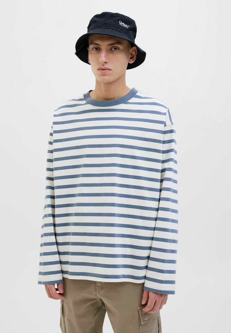 Gestreiftes Langarmshirt in Weiß und Hellblau, mit rundem Halsausschnitt und lockerer Passform. Kombiniert mit beigen Cargo-Hosen und einem schwarzen Bucket-Hut.