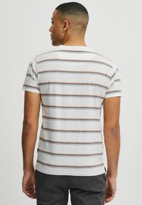 T-shirt kratkih rukava, s okruglim izrezom, u bijeloj boji s horizontalnim prugama u mornarskoj plavoj, hrđavoj i sivoj boji. Mekani materijal, blago prilagođen dizajn i detalj s bočnom etiketom.
