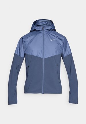 Μπλε σκούρο ναυτικό μπουφάν Nike με κουκούλα, με αντίθετο ανοιχτό μπλε πάνω μέρος, φερμουάρ και δύο πλαϊνές τσέπες. Λείο υλικό.