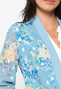 Světlomodrý květinový kimono s akcenty zlatých teček. Má měkkou, průhlednou látku s různými vzory květin a jednobarevným límcem.