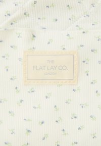 Blommönstrad tyg med en ljus krämfärgad bakgrund och små blå och gröna blommor, tillsammans med en etikett som säger "THE FLAT LAY CO. LONDON."