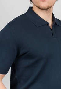 Námořnická modrá polo tričko s krátkým rukávem vyrobené z texturované pleteniny s klasickým límcem a dvouknoflíkovou légou, těsně padnoucí kolem trupu.
