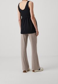 Haut sans manches noir avec un dos échancré et une taille cintrée, associé à un pantalon évasé côtelé beige clair. Chaussures décontractées visibles.