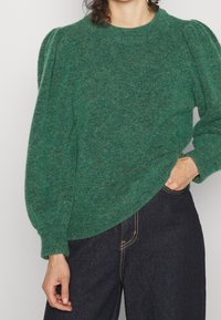 Grön, texturerad tröja med rund halsringning och puffärmar, matchad med mörk denim. Har ett mjukt, mysigt material och rena linjer.