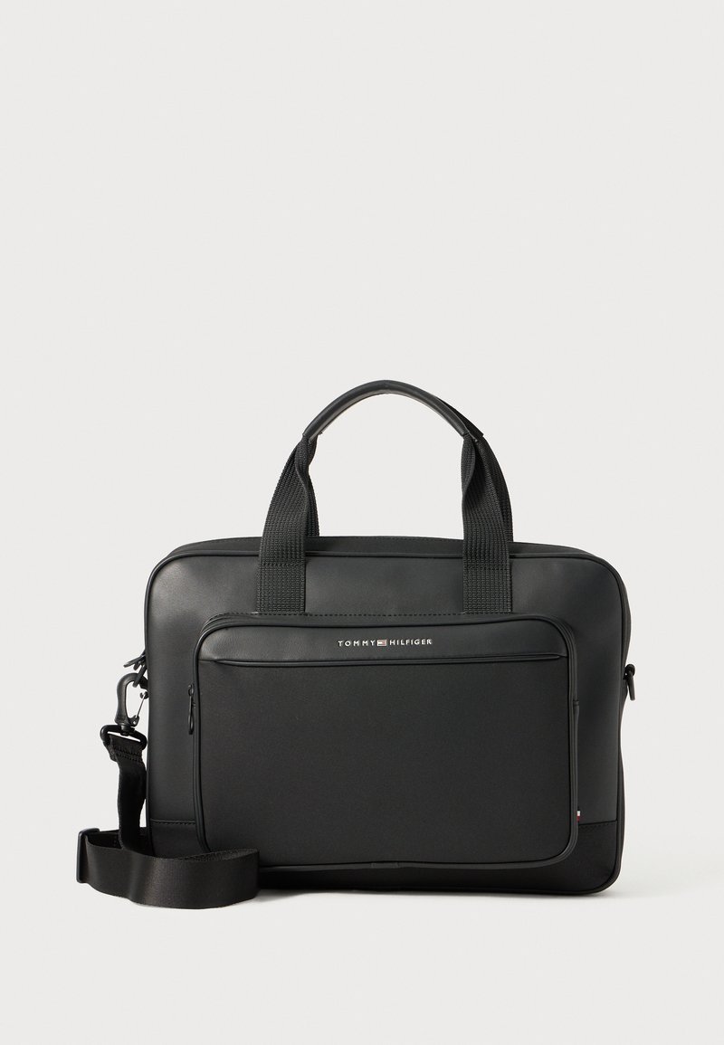 Sac à dos noir pour ordinateur portable avec une finition lisse, des poignées supérieures doubles, une sangle réglable, une poche zippée à l'avant et un détail logo argenté. Accents texturés visibles.
