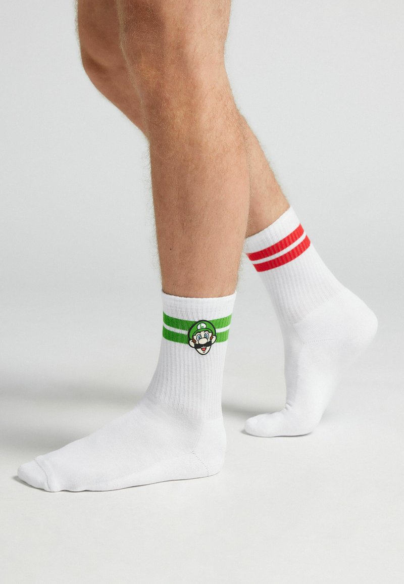 Calcetines de algodón blancos con rayas rojas y verdes en la parte superior, con un logo de personaje bordado en el costado.
