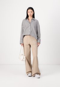 Striped button-up shirt with wide cuffs, paired with beige flared pants and white sneakers. Carries a small white handbag.
