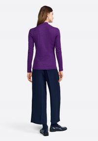 Top lung cu mâneci lungi, ajustat, de culoare mov, dintr-un material texturat, cu guler înalt; asociat cu pantaloni largi de culoare închis și pantofi negri. Design simplu, fără modele vizibile.