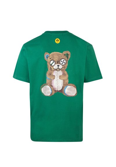 T-shirt in cotone verde con una grafica di un orso cartoon sul retro, con toppe cucite e occhi simili a bottoni. Accentuato con un'etichetta gialla.