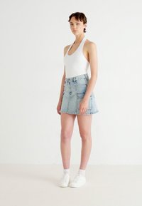 Fustă mini din denim de culoare albastru deschis, cu talie înaltă, închidere cu nasture și fermoar, buzunare frontale și tiv desfăcut. Asortată cu un top alb fără mâneci.