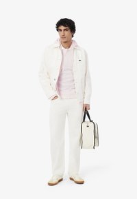Giubbotto di jeans crema, felpa a strisce rosa chiaro, pantaloni bianchi e sneakers beige. Tiene una borsa bianca con accenti neri.