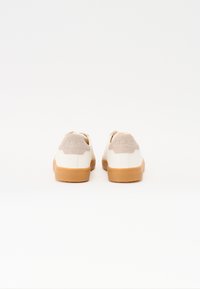 Sneakers bianchi con un inserto in suede beige testurizzato sul tallone e una suola in gomma color caramello. Il nome del marchio "CLAE" è impresso sul tallone.