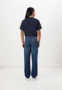 Marineblå T-skjorte med korte ermer, parret med løstsittende blå jeans med denimstruktur og to baklommer, brukt med hvite joggesko.