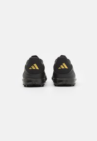 Zapatillas deportivas negras con un diseño elegante, que presentan una parte superior texturizada, un destacado logo dorado de Adidas en los talones, y una suela duradera para agarre.