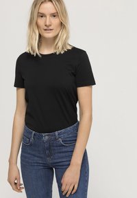 Svart kortärmad t-shirt i kombination med högmidjade blå denimjeans. T-shirten har rund halsringning och en slät, tight passform.