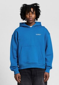 Blue hoodie made of soft fabric, featuring a kangaroo pocket and ribbed cuffs. White print text on the left chest area.