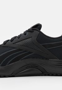 Černá sportovní bota s vrchní částí ze síťoviny a syntetického materiálu, vybavená podporou klenby, texturovaným povrchem a elegantním designem se šňůrkami.