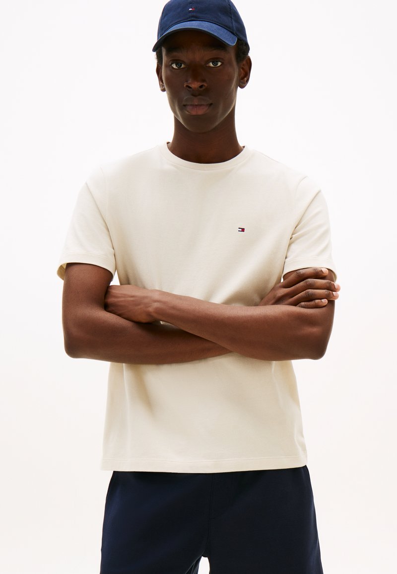 Beežist puuvillast lühikeste varrukatega ja ümar kaelusega T-särk, millel on rinnal väike logo punase, valge ja sinise värviga.