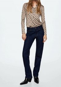 Braun gemustertes Langarmhemd mit geometrischem Design, kombiniert mit dunkelblauen Jeans im Straight-Leg-Schnitt und schwarzen spitzen Stiefeln.