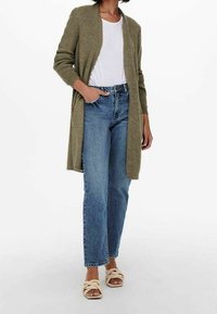 Olive green knit cardigan over a white T-shirt, paired with light blue straight-leg jeans and cream braided slide sandals.