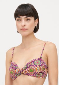 Veelkleurige bikini-top met een gedraaide voorkant. Kenmerkt zich door ingewikkelde bloempatronen in paars, groen, oranje en geel. Verstelbare bandjes.