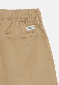 Kašmirne hlače boje khaki s elastičnim pojasom, stražnjim džepom i oznakom "JACK & JONES EST. 1990" blizu gornjeg ruba. Tekstura na površini.
