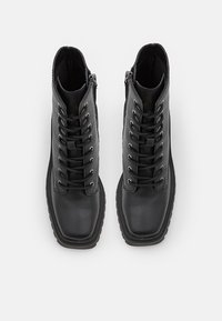 Paire de bottines en cuir noir à lacets avec fermetures éclair latérales et semelles épaisses, vues de dessus sur fond blanc.