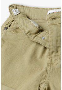 Pantalons en coton beige clair dotés d'une fermeture par bouton, de détails de couture et de poches latérales. Le tissu a une texture lisse et un léger éclat.