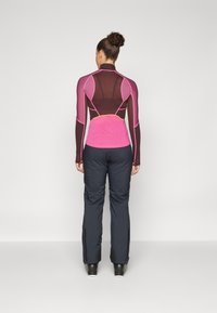 Maglia sportiva a maniche lunghe con una combinazione di colori rosa e marrone, con pannelli in rete. Abbinate a pantaloni aderenti blu scuro.
