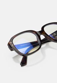 Brązowe okulary w kratkę z grubymi prostokątnymi oprawkami, niebieskimi soczewkami oraz małymi metalowymi akcentami z przodu. Logo widoczne wewnątrz.