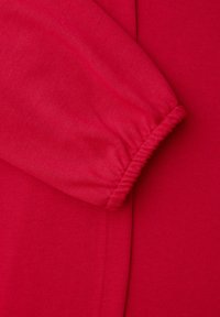 Červený látkový návlek s elastickým lemem složený přes jednobarevné červené pozadí.