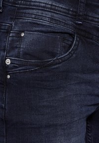 Dark blue denim jeans with a smooth texture. Features a front pocket, metal rivets, and subtle stitching on the waistband.