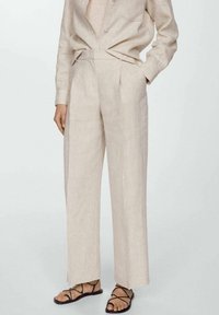 Pantalons en lin beige à taille haute, avec des plis, des poches latérales et une coupe droite, assortis à un haut à boutons du même coloris.