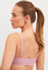 Lichtroze beha met verstelbare bandjes en een gladde, textuurstof. Heeft een eenvoudig ontwerp en minimale hardwareaccenten.