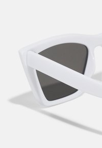 Bílé sluneční brýle s ostrým designem, tmavými skly a hladkým povrchem. Acetátový rám a nožičky, které mají minimalistický styl.