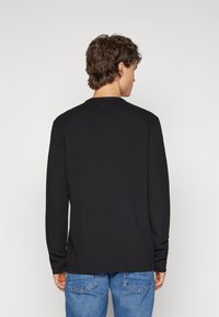 Zwarte longsleeve shirt met een ronde halslijn, gemaakt van een soepele stof. De achterkant vertoont minimale naden en een subtiele zoomdetail.