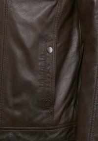 Braune Lederjacke mit glatter Textur, sichtbaren Nähten und metallischen Druckknopf-Details an der Vorderseite der Tasche.