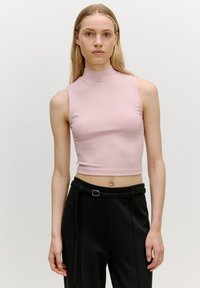 Lichtroze geribde mouwloze top met een hoge halslijn, gecombineerd met zwarte hoge taille broeken met een riem en plooien aan de voorkant.