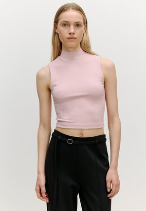 Lichtroze geribde mouwloze top met een hoge halslijn, gecombineerd met zwarte hoge taille broeken met een riem en plooien aan de voorkant.