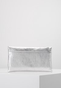 Pochette rectangulaire argentée brillante avec une légère pliure, posée sur une surface blanche devant un fond gris clair.