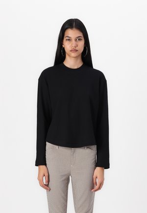 Svart langermet topp med rund hals og avslappet passform. Laget av mykt materiale, har den en cropped stil og er kombinert med rutete bukser.